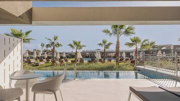 A poolside area with lounge chairs, a table, and a view of a pool and palm trees.