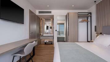 Een moderne hotelkamer met een bureau, stoel, bed en een inloopkast met spiegel en hanggedeelte.