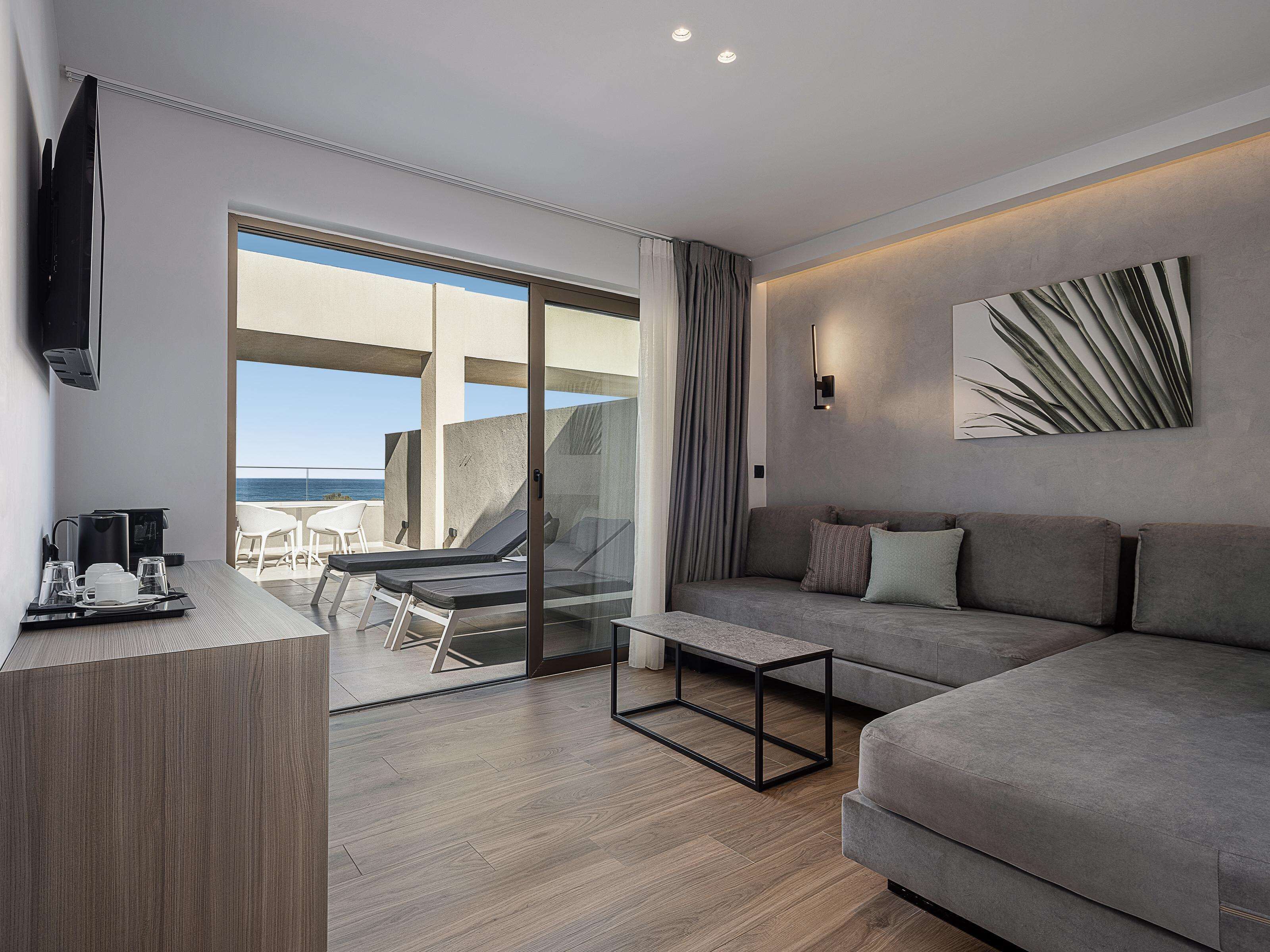 Una habitación de hotel moderna con balcón, un sofá, una mesa de centro y un televisor.