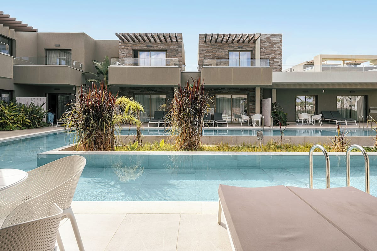 A modern hotel with a swimming pool, lounge chairs, and a patio area.