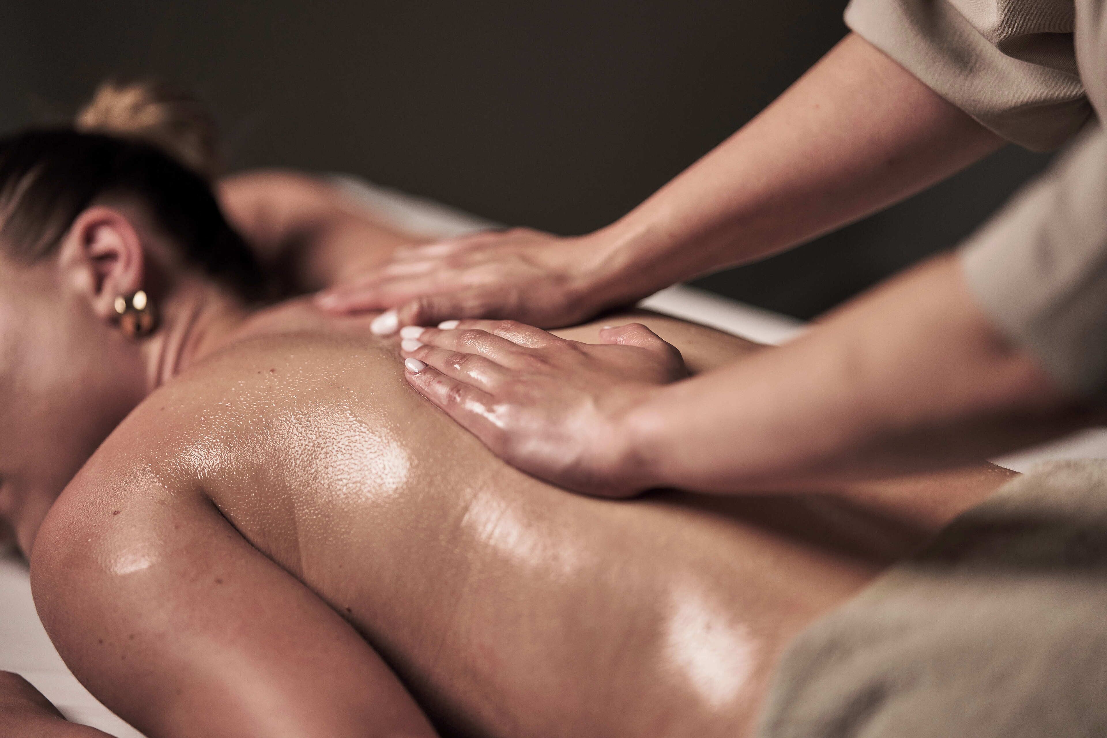 En pågående massagebehandling, där fokus ligger på massörens händer och klientens rygg.