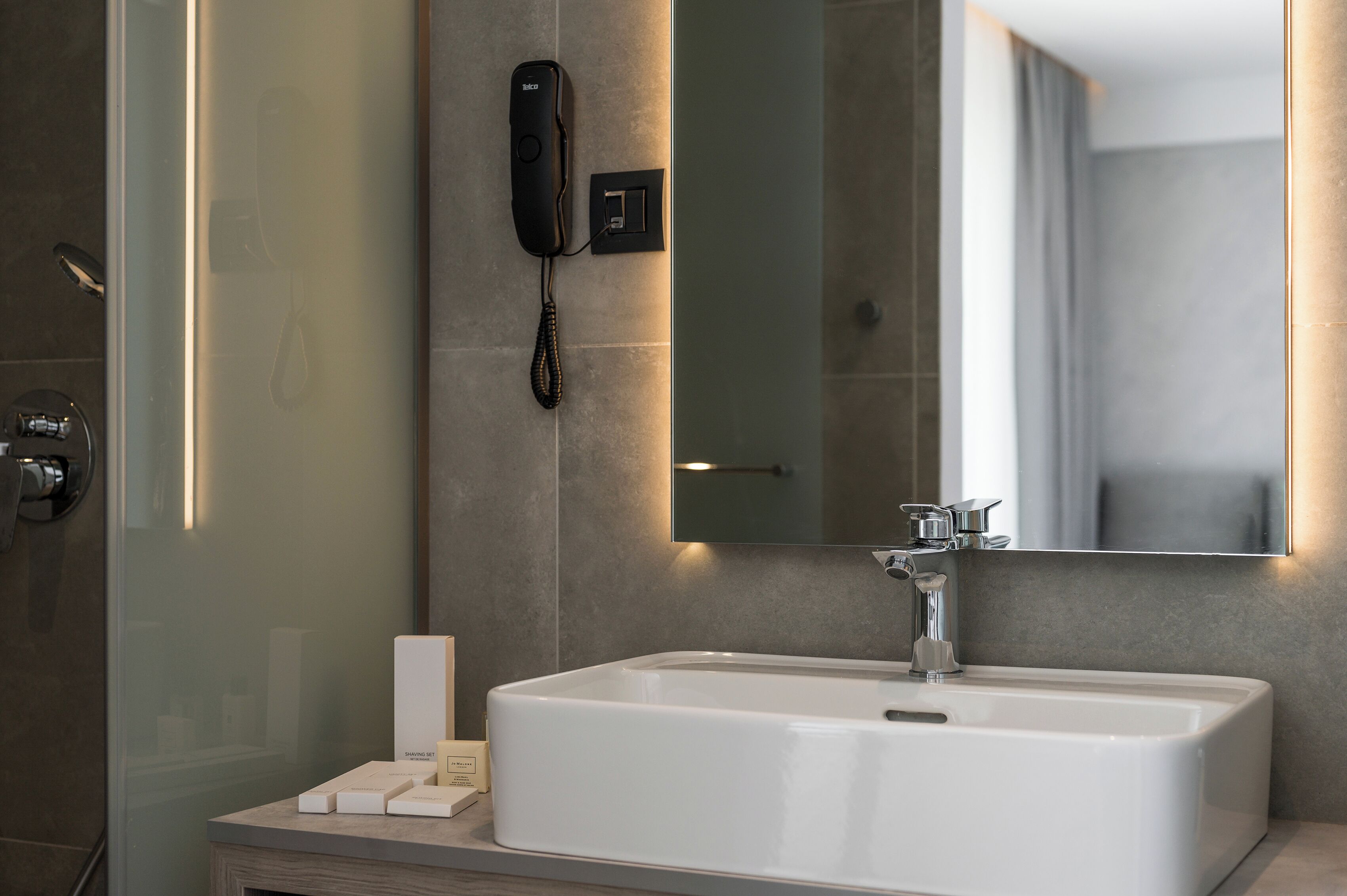 Un baño moderno con un lavamanos blanco, un espejo y un teléfono instalado en la pared.