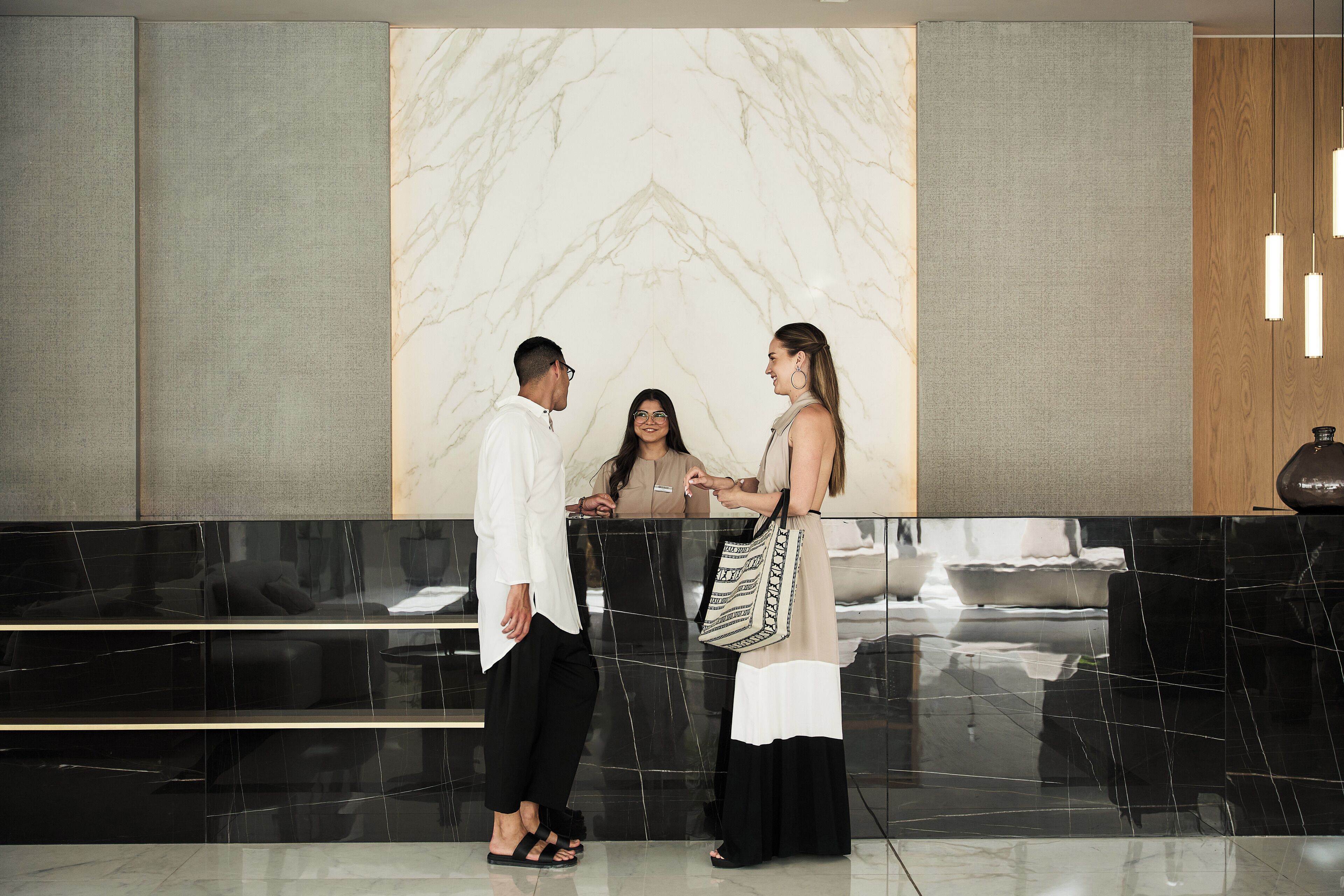 A reception area with a marble wall, a black reception desk, and a wooden panel on the right.
