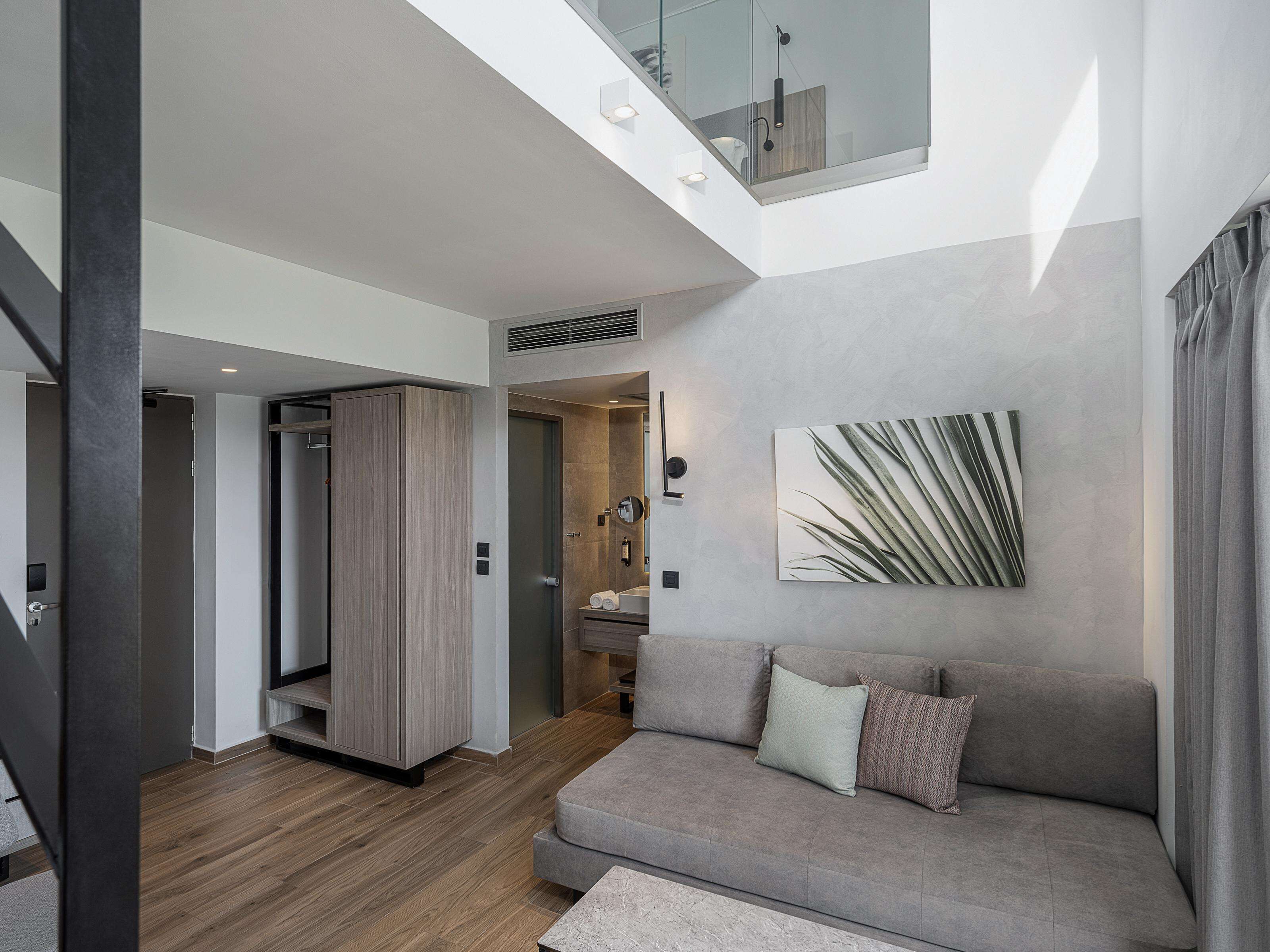 A modern living room with a grey sofa, a wooden floor, and a large window.