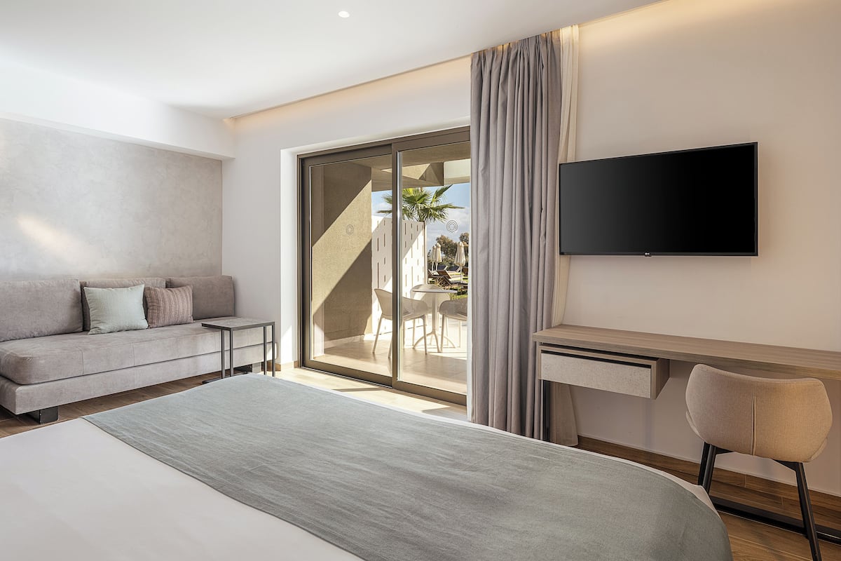 A modern hotel room with a bed, a desk, a TV, and a balcony with outdoor furniture.