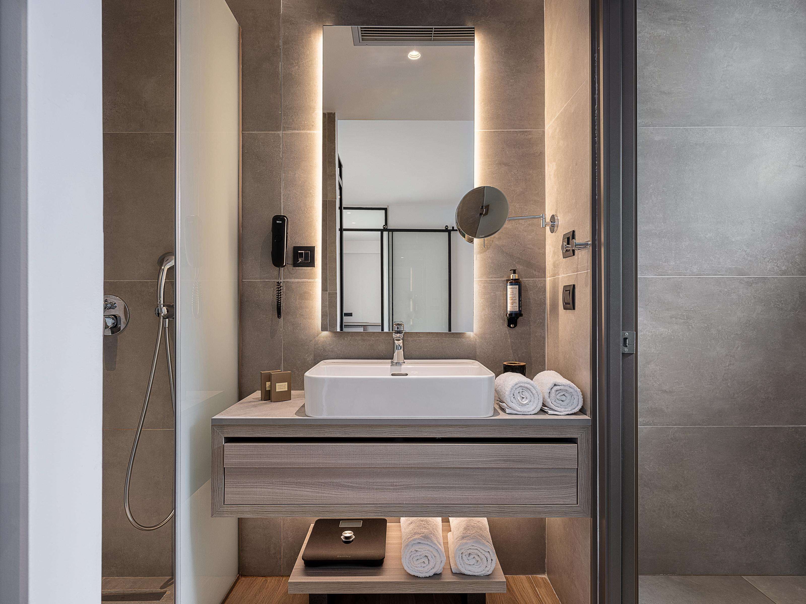 Een moderne badkamer met een inbouwwastafel, een spiegel, een handdouche en netjes opgerolde handdoeken op een houten plank.