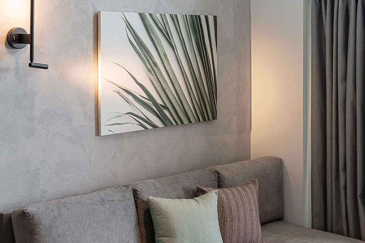 A modern living room with a grey sofa, a wall-mounted light, and a framed plant.