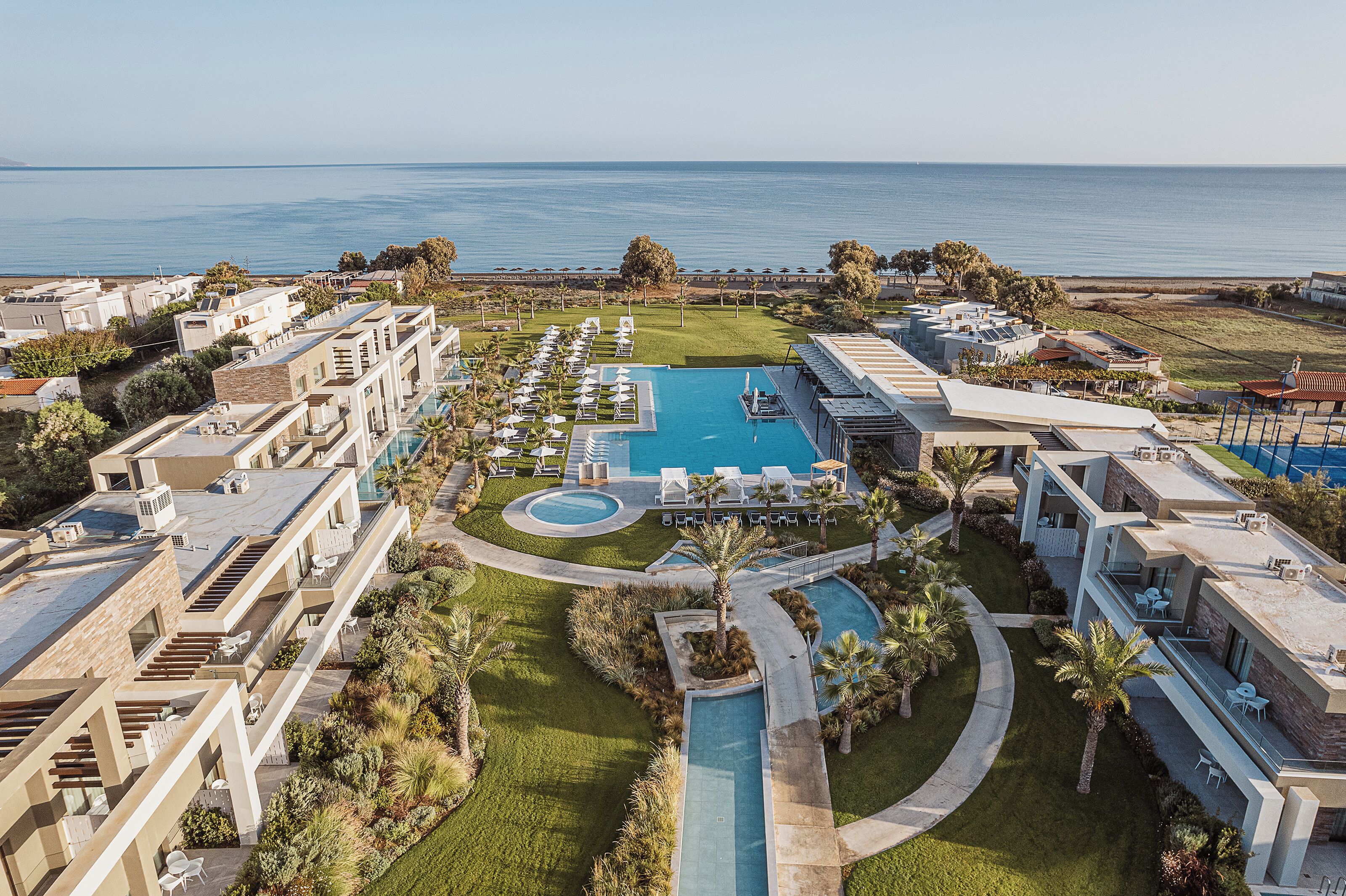 A resort with multiple swimming pools, a well-maintained lawn, and a view of the ocean.