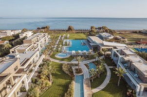 A resort with multiple swimming pools, a well-maintained lawn, and a view of the ocean.