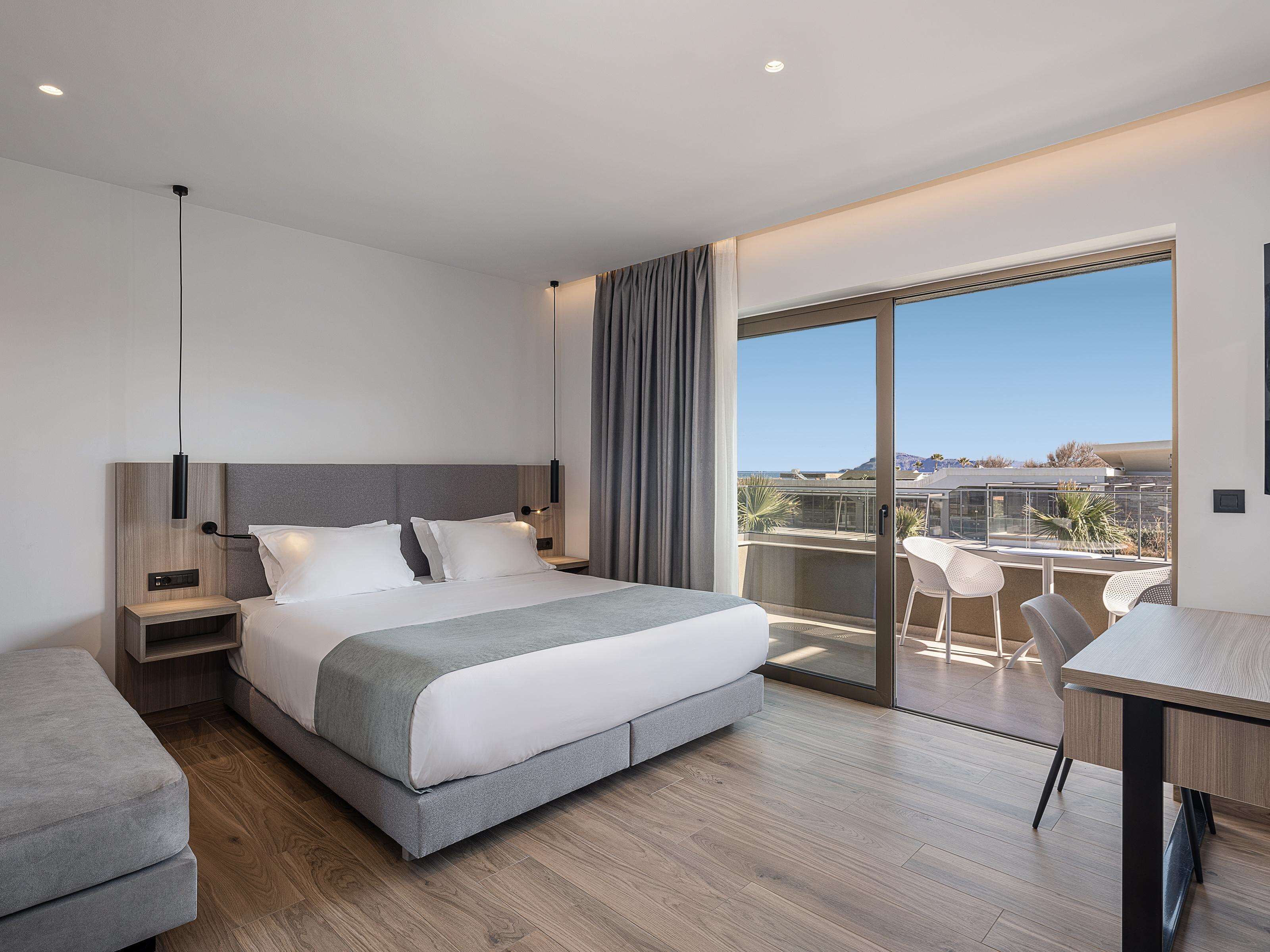 A modern hotel room with a large bed, bedside tables, a desk, and a balcony with a view.