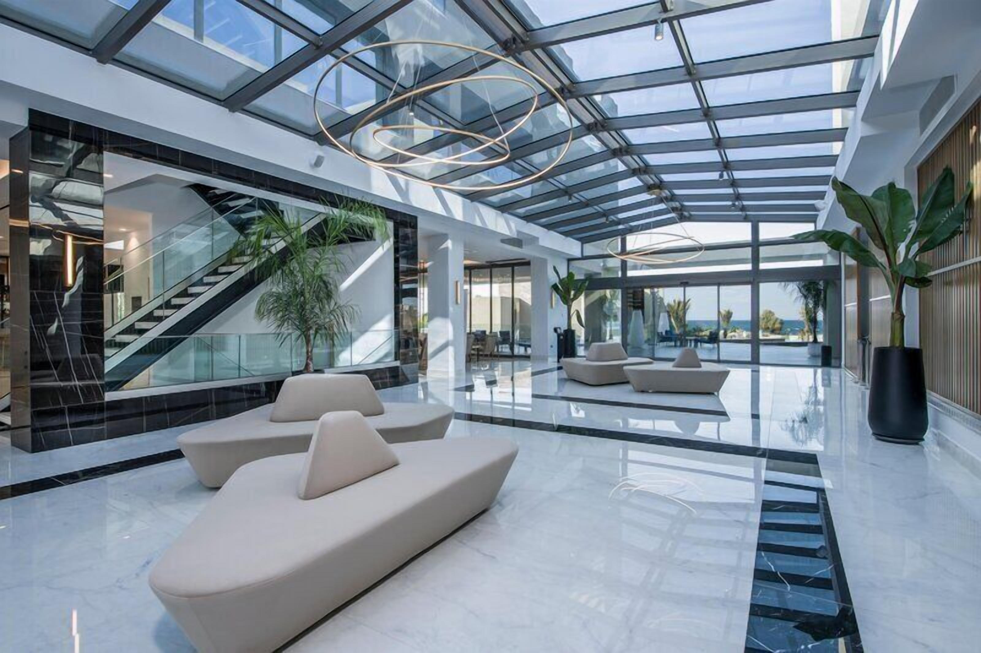 A spacious lobby with a glass ceiling, a staircase, and seating areas.