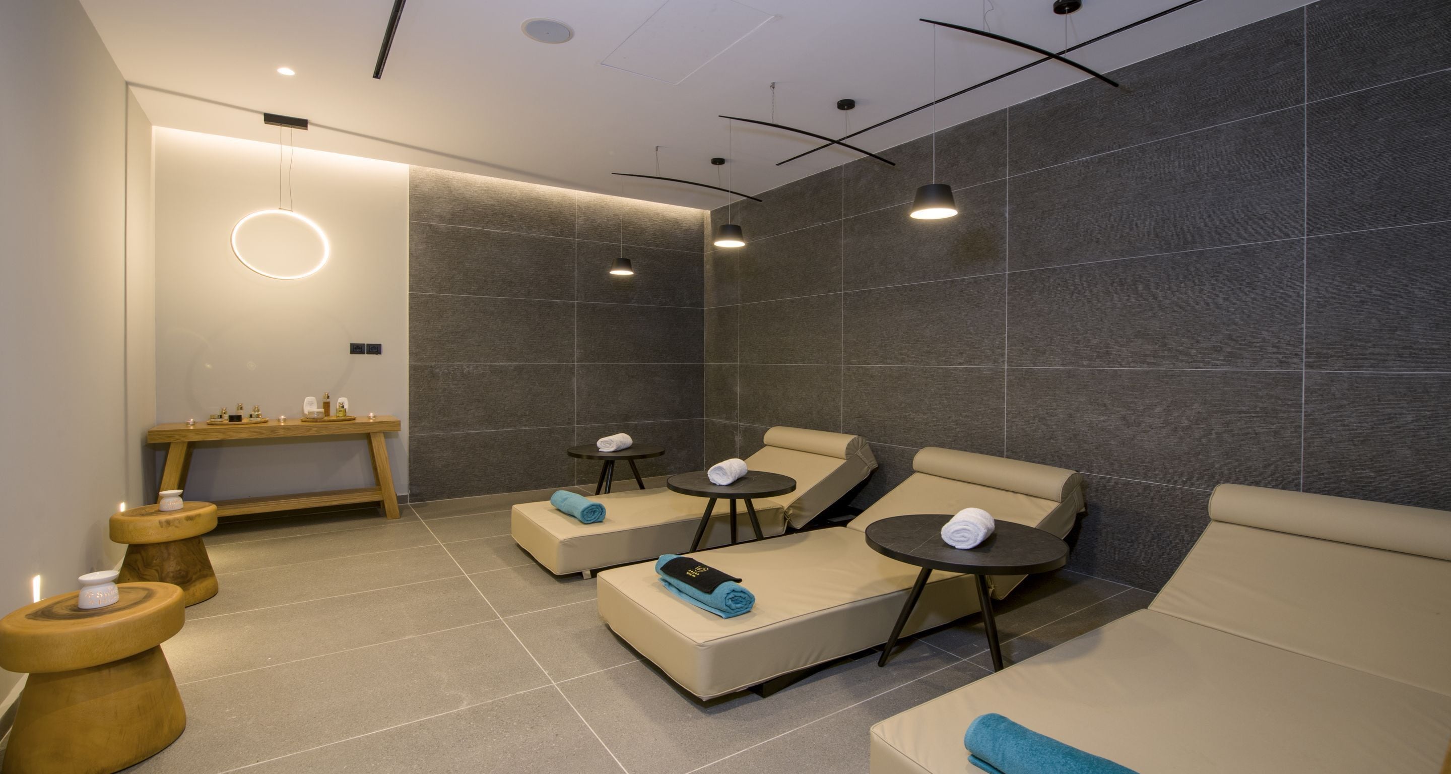 Ein Wellnessraum mit drei Massagetischen, einer Holzbank und einem Tisch mit Kerzen.