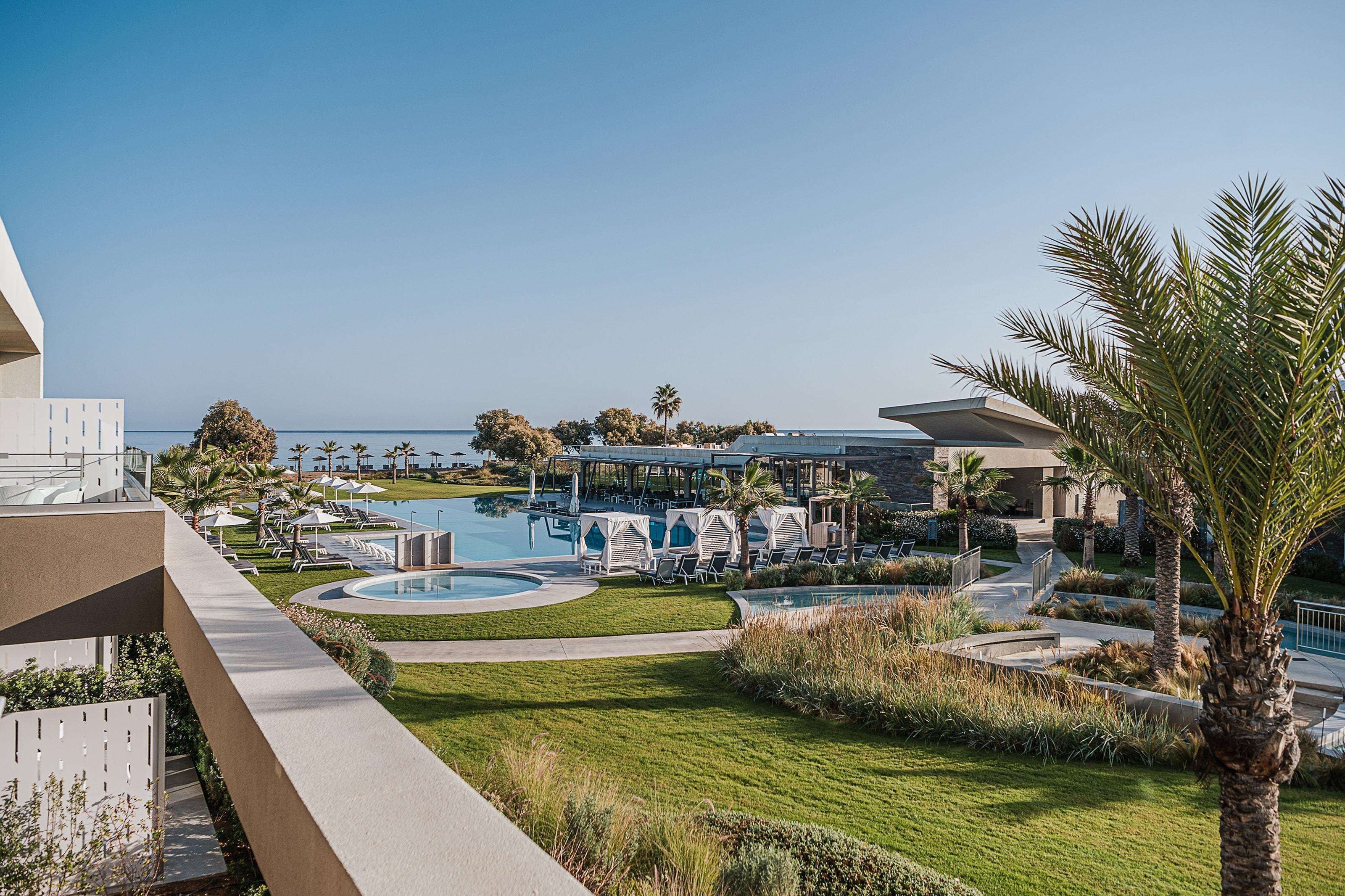 A resort with a swimming pool, lounge chairs, palm trees, and a view of the ocean.