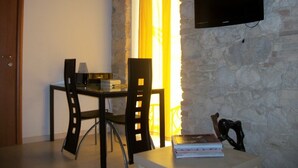 A dining area with a stone wall, a TV mounted on the wall, and a window with yellow curtains. - Colle di Minerva Entire Apartment (Chieti)