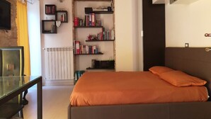 A bedroom with a brick wall, a bed with an orange bedspread, a bookshelf, and a radiator. - Colle di Minerva Entire Apartment (Chieti)