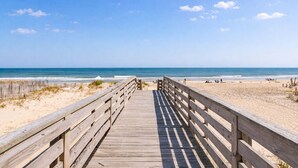 A wooden boardwalk leading to a beach with clear skies. - Oceanfront luxury in this spacious 10-bedroom home in South Nags Head. (South Nags Head)