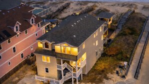 A beachfront property with a large house featuring a balcony and a staircase leading to a deck. - Oceanfront luxury in this spacious 10-bedroom home in South Nags Head. (South Nags Head)