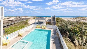 A pool area with a clear view of the beach and ocean, wooden deck, and beach chairs. - Oceanfront luxury in this spacious 10-bedroom home in South Nags Head. (South Nags Head)