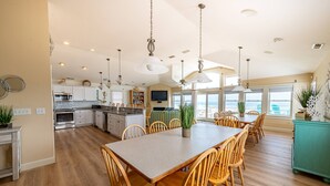 A spacious kitchen with wooden cabinets, a dining table with chairs, and a large window offering a view. - Oceanfront luxury in this spacious 10-bedroom home in South Nags Head. (South Nags Head)