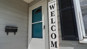 Entrada d'una casa amb un rètol de 'WELCOME', una closca de correu i una porta amb una finestra.