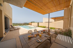 Ein Essbereich mit Blick auf einen Pool, Holzmöbel und ein für eine Mahlzeit gedeckter Tisch.