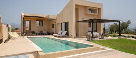 A modern house with a swimming pool, outdoor seating, and a covered patio area.