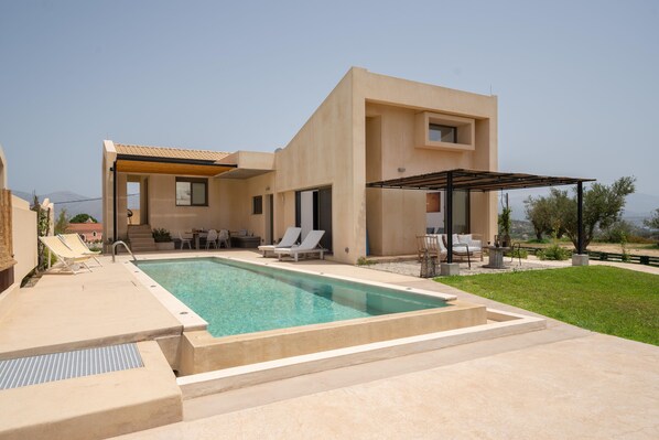 A modern house with a swimming pool, outdoor seating, and a covered patio area.