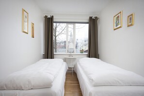 Ein Zimmer mit zwei Einzelbetten, einem kleinen Tisch und einem Fenster mit Vorhängen.