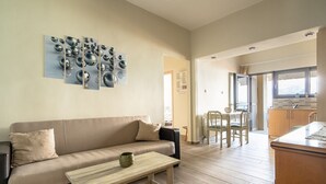 A modern living room with a beige sofa, a wooden coffee table, and a kitchen area visible through an open door. - Zoi Studios (Kefalonia)