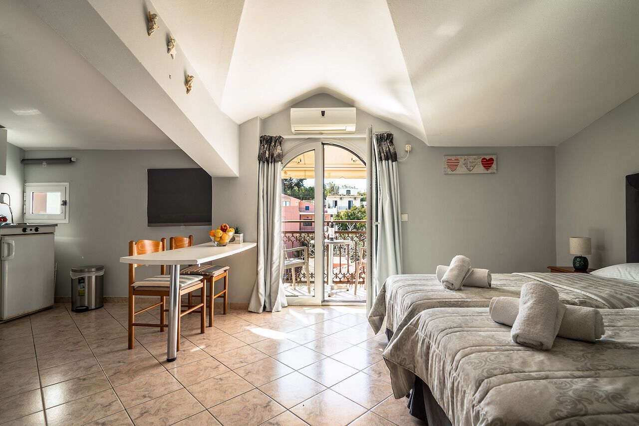 A bedroom with two beds, a desk, and a balcony.