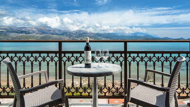 A balcony with a table, two chairs, and a bottle of wine. - Zoi Studios (Kefalonia)