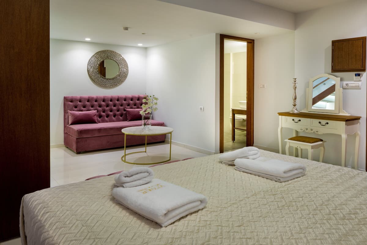 Une chambre d’hôtel avec un grand lit, un canapé rose, une petite table ronde et un miroir au-dessus d’une coiffeuse.