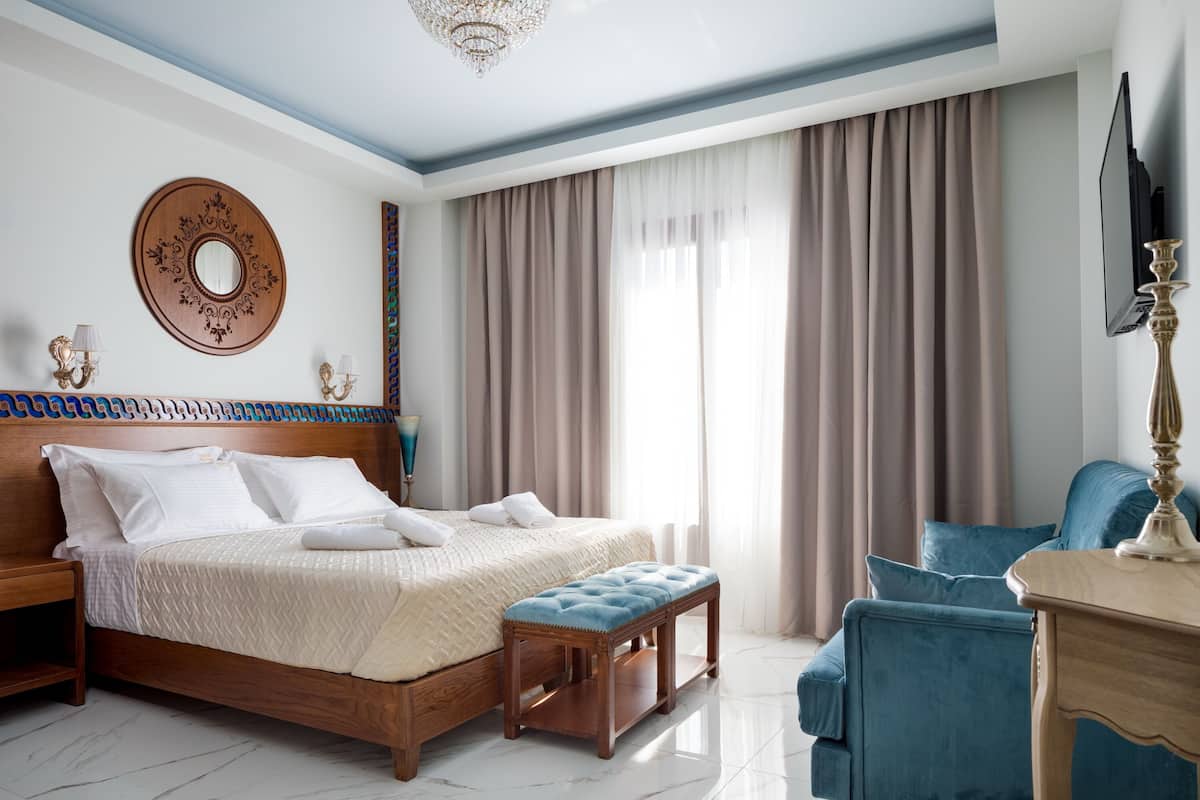 Une chambre à coucher avec un lit en bois, un miroir rond, un fauteuil bleu et un téléviseur posé sur un meuble.