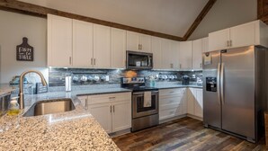 Una cocina con armarios blancos, un refrigerador de acero inoxidable, un microondas y un horno.