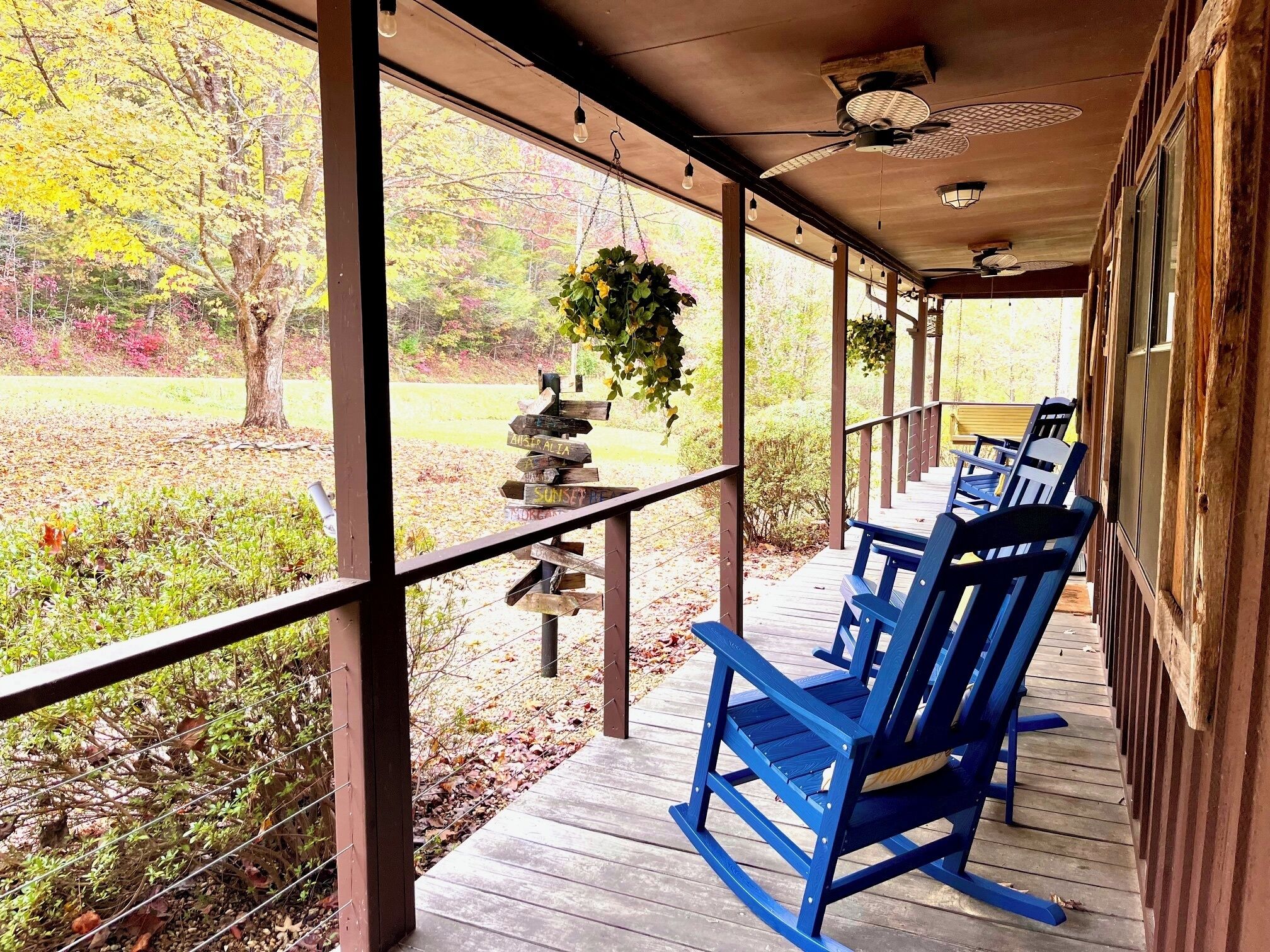 A covered porch with blue chairs, a hanging plant, and a wooden sign with directions.