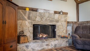 A stone fireplace with a sign above it, a wooden cabinet to the left, and a grey armchair to the right.