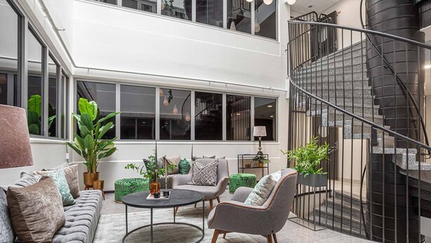 A spacious living area with a sofa set, a coffee table, and a chair. There is a staircase with a metal railing leading to an upper level.