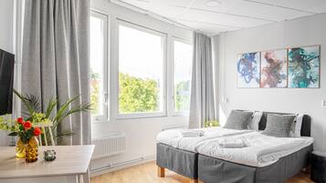 A modern bedroom with a large bed, a small table with a vase of flowers, and a window with curtains.