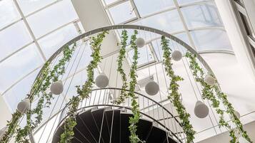 A spiral staircase with a glass ceiling, surrounded by greenery and spherical light fixtures.