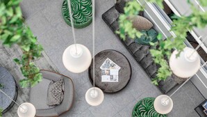 A modern outdoor seating area with round tables, green patterned cushions, and hanging pendant lights.