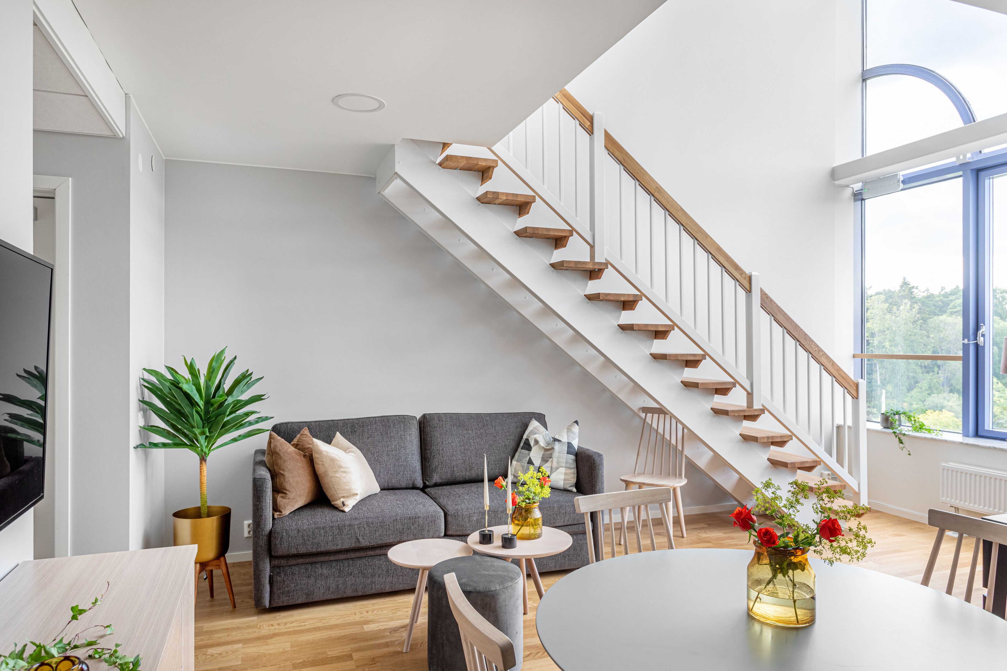 Un salón moderno con sofá gris, escalera de madera y comedor con una mesa redonda.