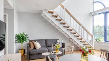 Un salón moderno con sofá gris, escalera de madera y comedor con una mesa redonda.