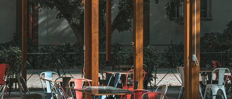 An outdoor cafe with tables and chairs, large windows, and a wooden pergola.