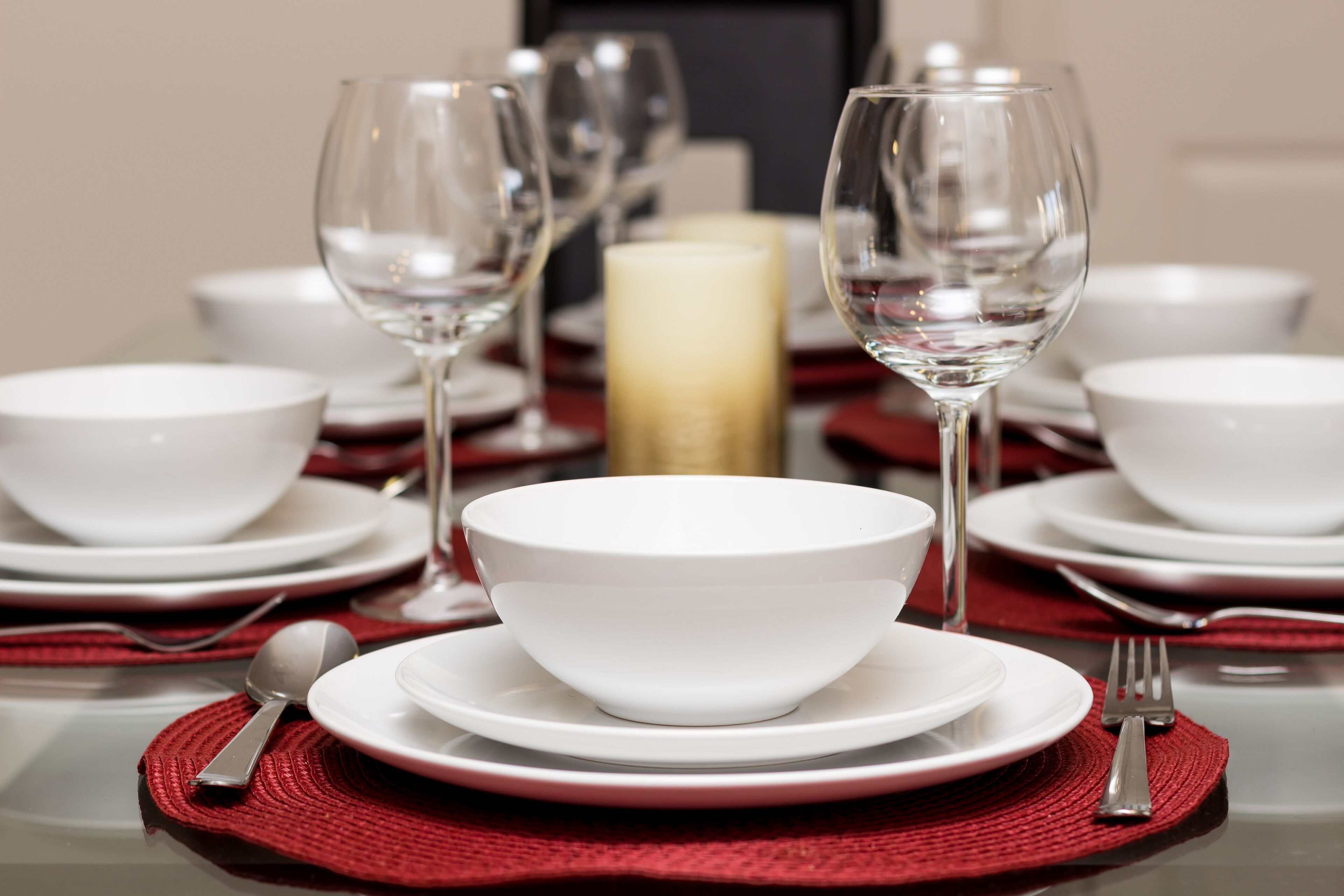 A table set for dining with white plates, bowls, and wine glasses, and a candle centerpiece.