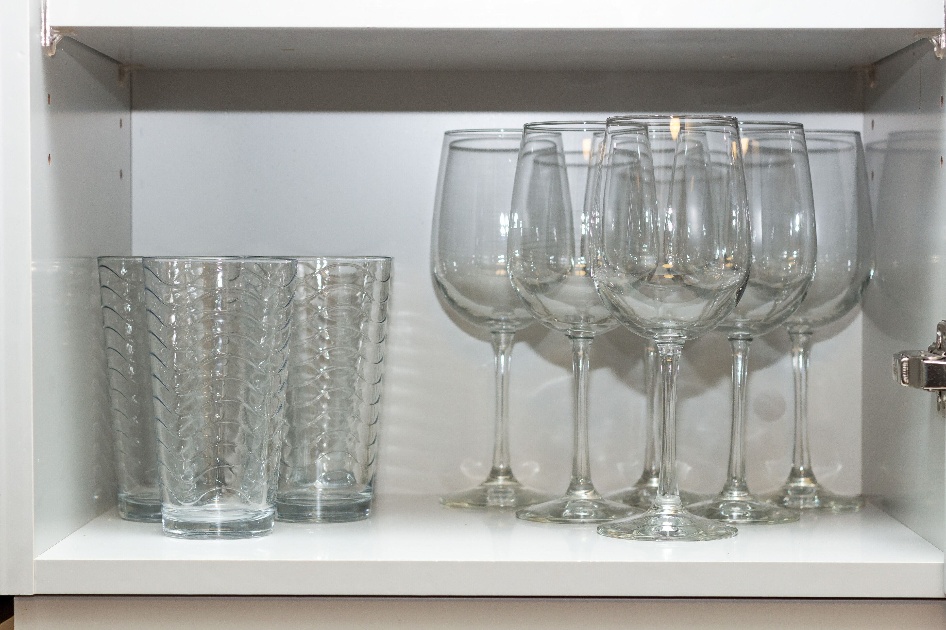 A cabinet with clear glassware, including tumblers and wine glasses, arranged neatly.