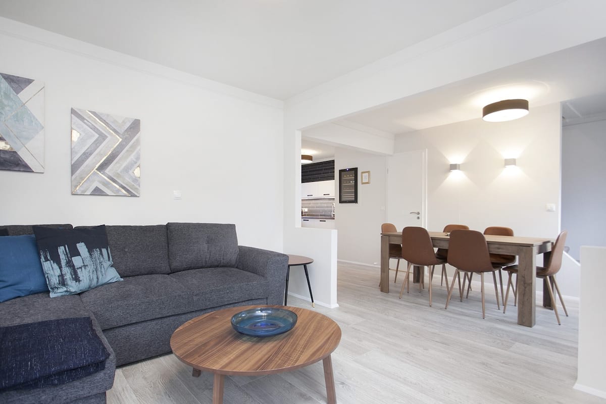 A modern living room with a grey sofa, a round wooden coffee table, and a dining area with a wooden table and chairs.