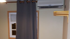 Una camera da letto con un letto, una finestra con tenda, un condizionatore e una porta con maniglia.