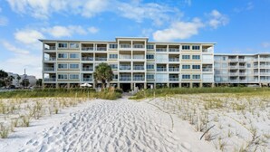 Hotel frente a la playa con varios balcones, una playa arenosa frente a él y un cielo despejado.