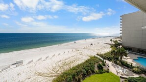 Vista a la playa desde un balcón de hotel con piscina y sillones de descanso.