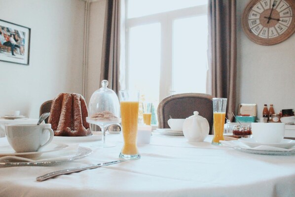 Una mesa de desayuno con una taza de café, un vaso de jugo de naranja, un vaso de leche, un calentador de té y un plato de pasteles.